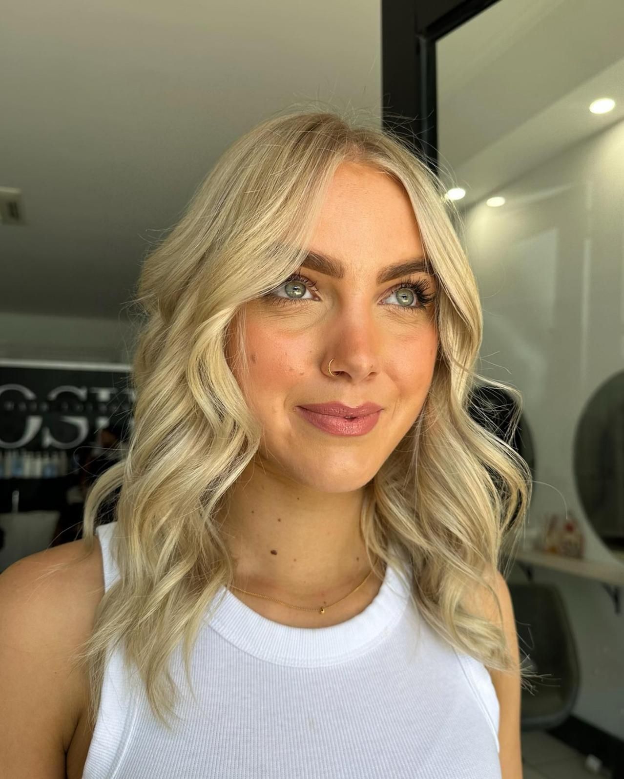 A Woman with Blonde Hair Is Wearing a White Tank Top and Smiling — Losh Hair Lounge In Toowoomba City, QLD