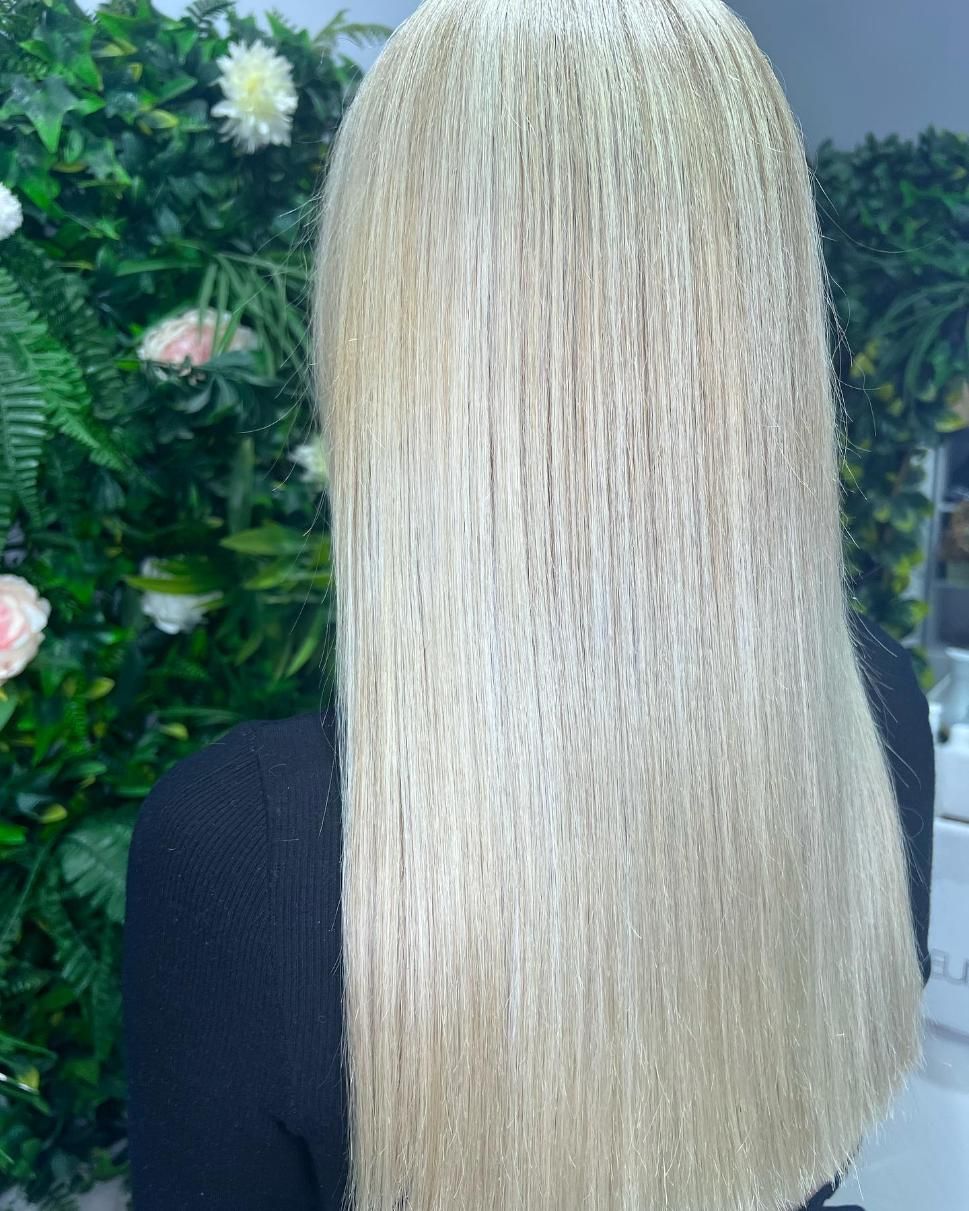 A Woman with Long Blonde Hair Is Standing in Front of A Wall of Flowers — Losh Hair Lounge In Toowoomba City, QLD