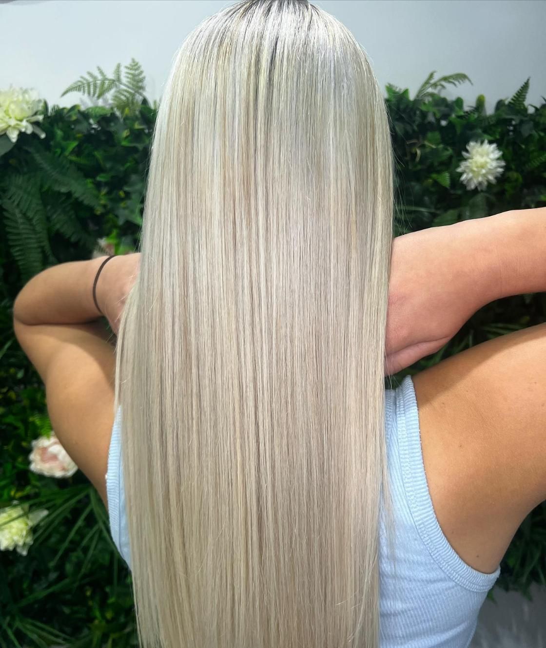 A Woman with Long Blonde Hair Is Standing in Front of A Wall of Flowers — Losh Hair Lounge In Toowoomba City, QLD