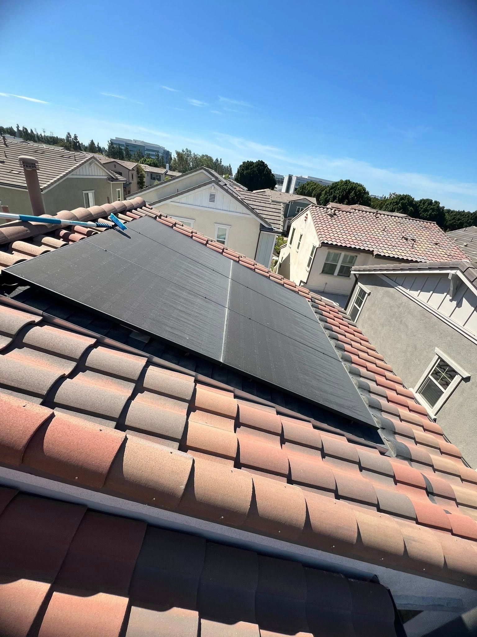 Solar panels installed on a residential roof with terracotta tiles, under a clear blue sky.