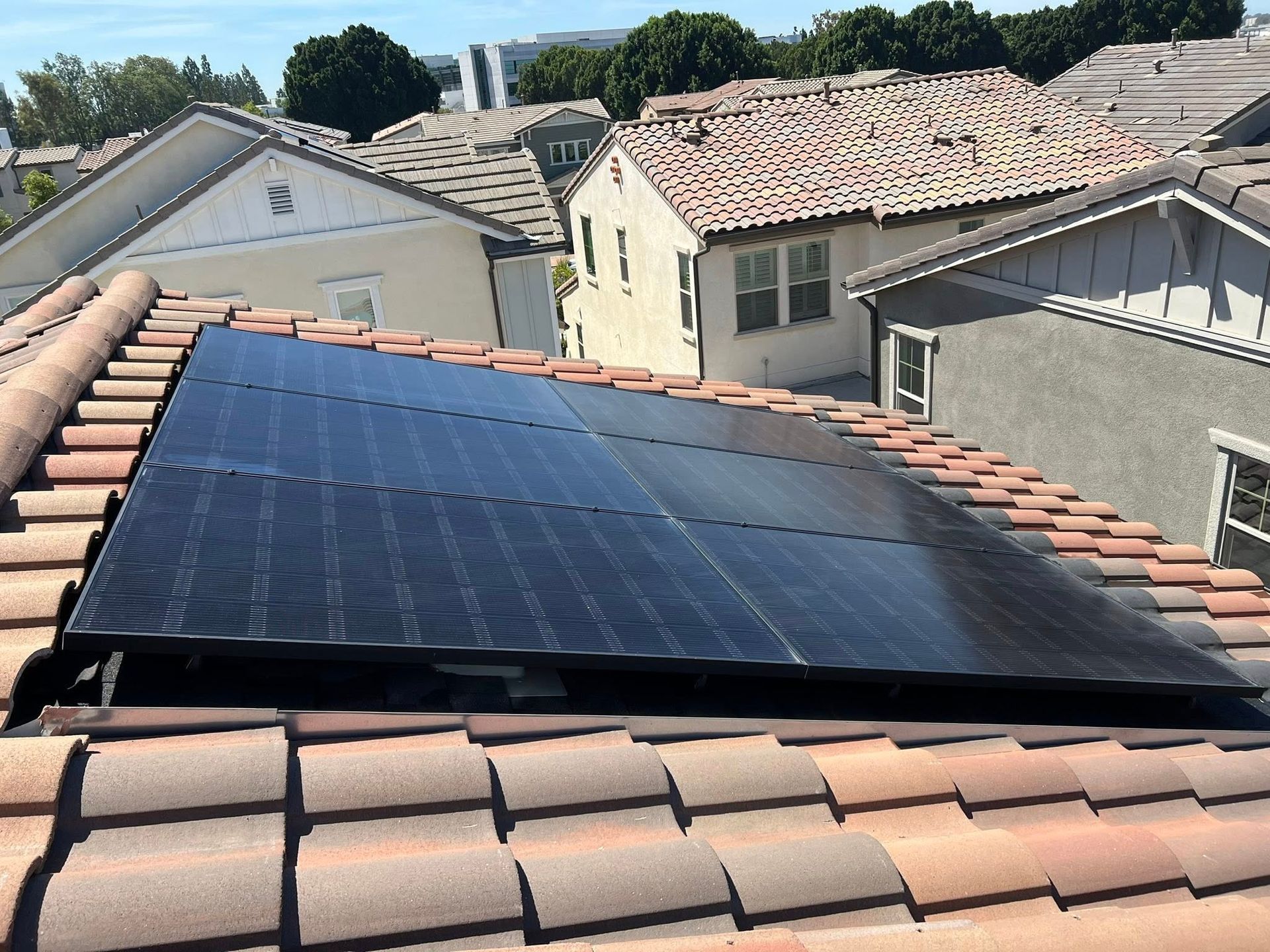 A rectangular array of black solar panels installed on a sloped, terracotta-tiled residential roof under a sunny sky.