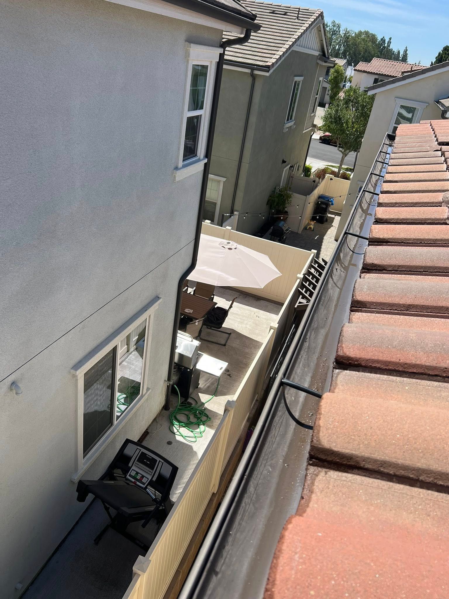 A high-angle view looking down from a tiled roof onto a side yard with a patio area and a small folding chair.