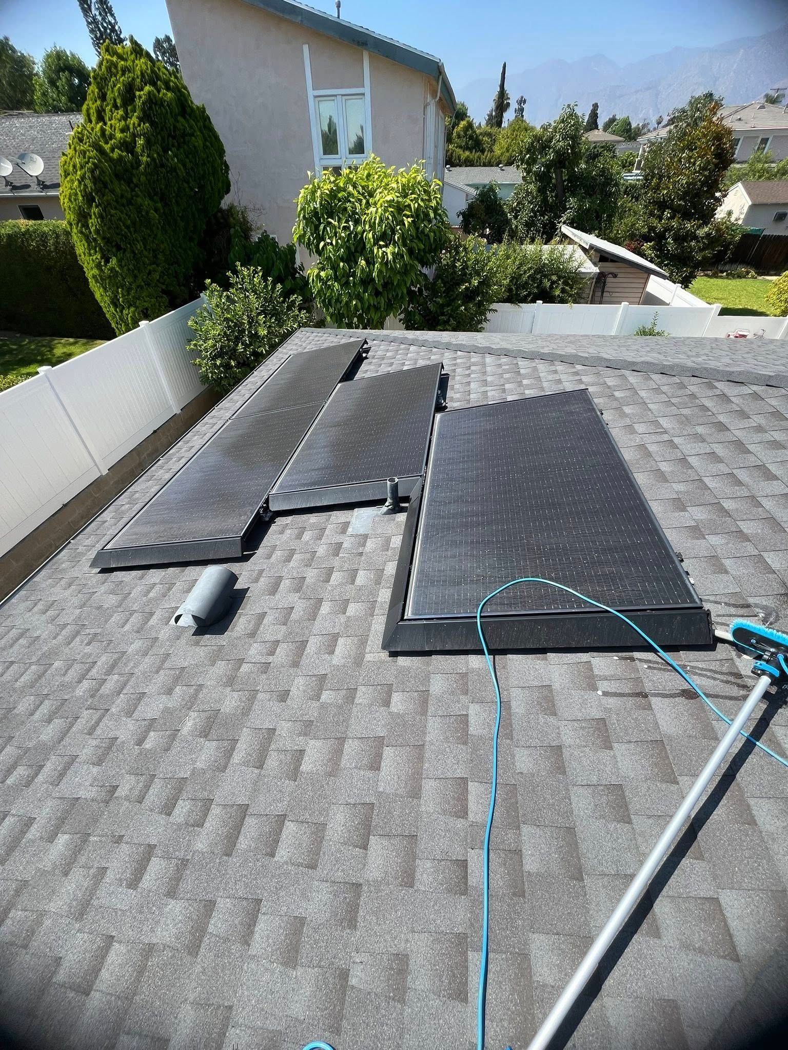 Three black solar pool heating panels arranged on a gray shingled roof with a cleaning pole in the foreground.