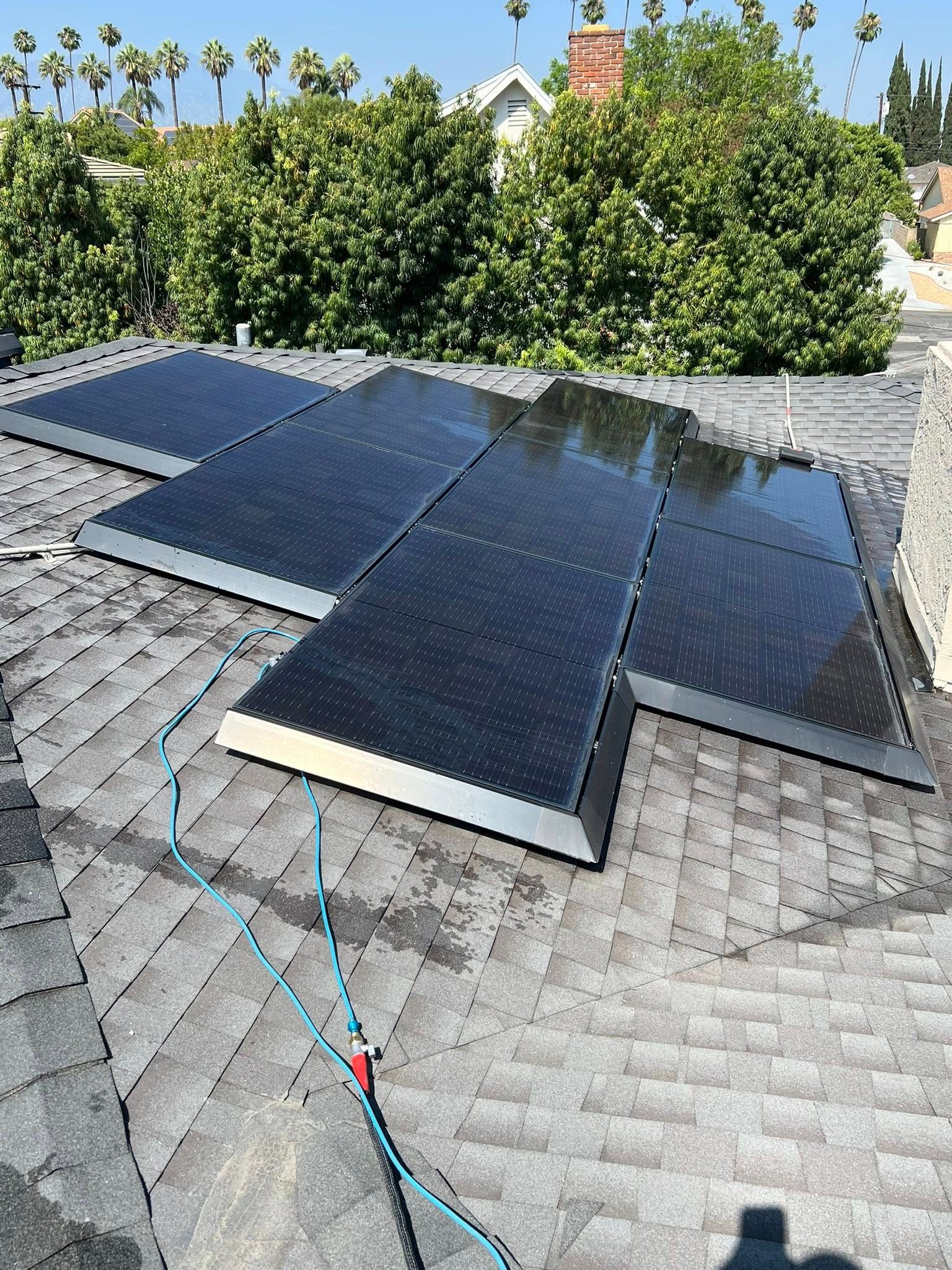 Four black solar panels installed on a grey shingled roof with blue wiring visible on the surface.