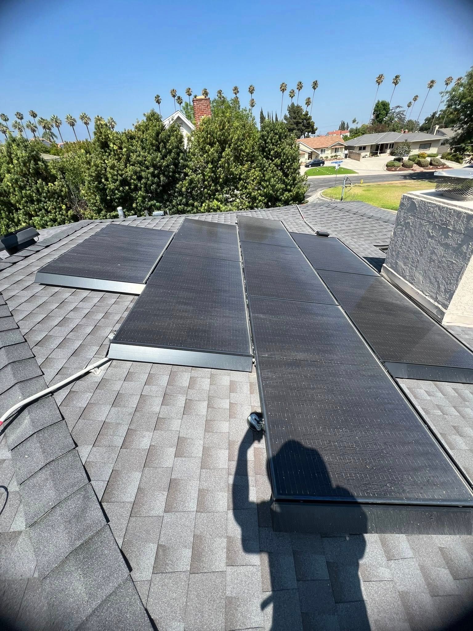 A high-angle view of solar panels installed on a grey asphalt-shingled residential roof on a sunny day.