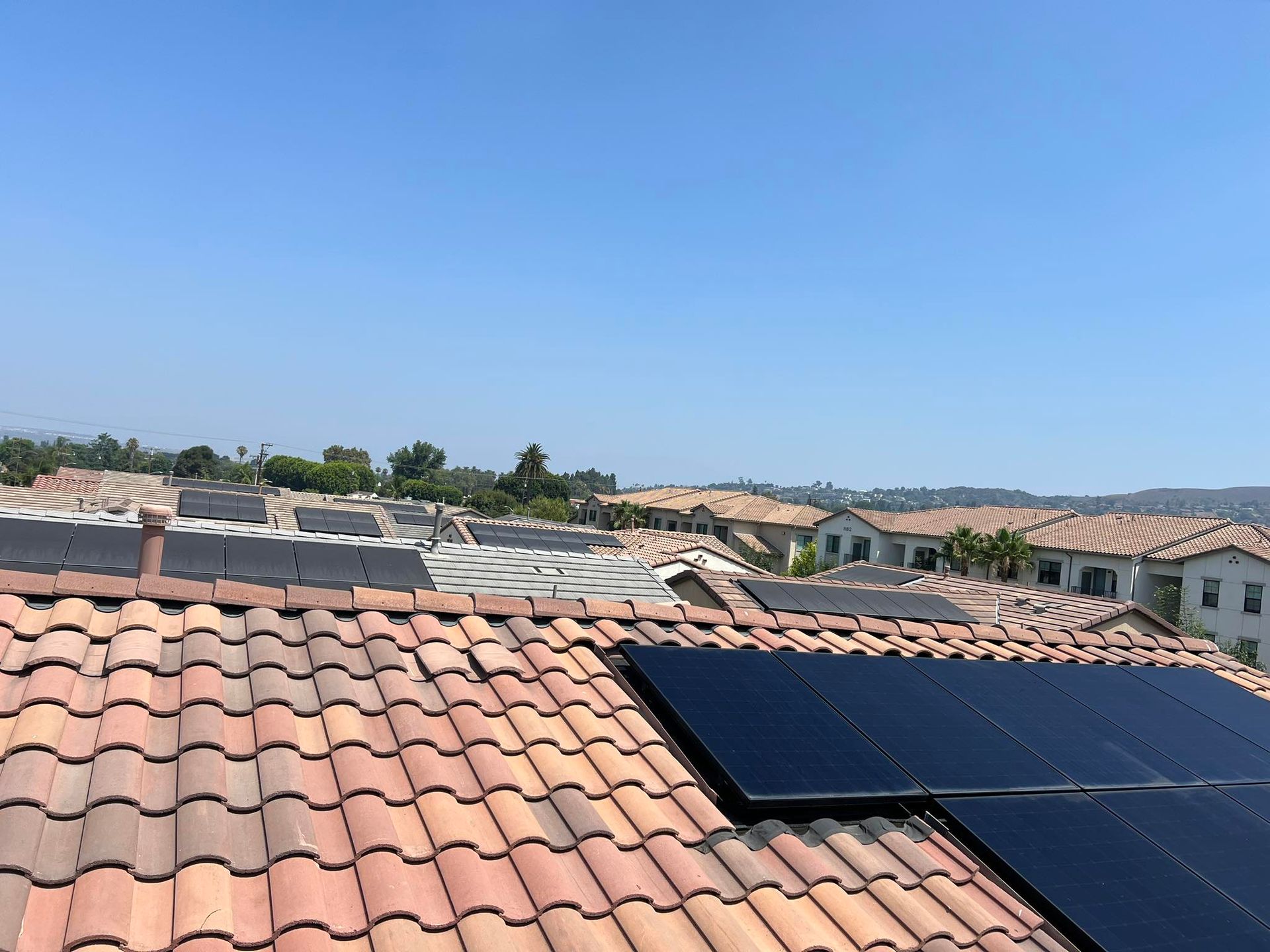 A view of terracotta-tiled roofs under a clear blue sky, featuring solar panels on some homes in a suburban neighborhood.