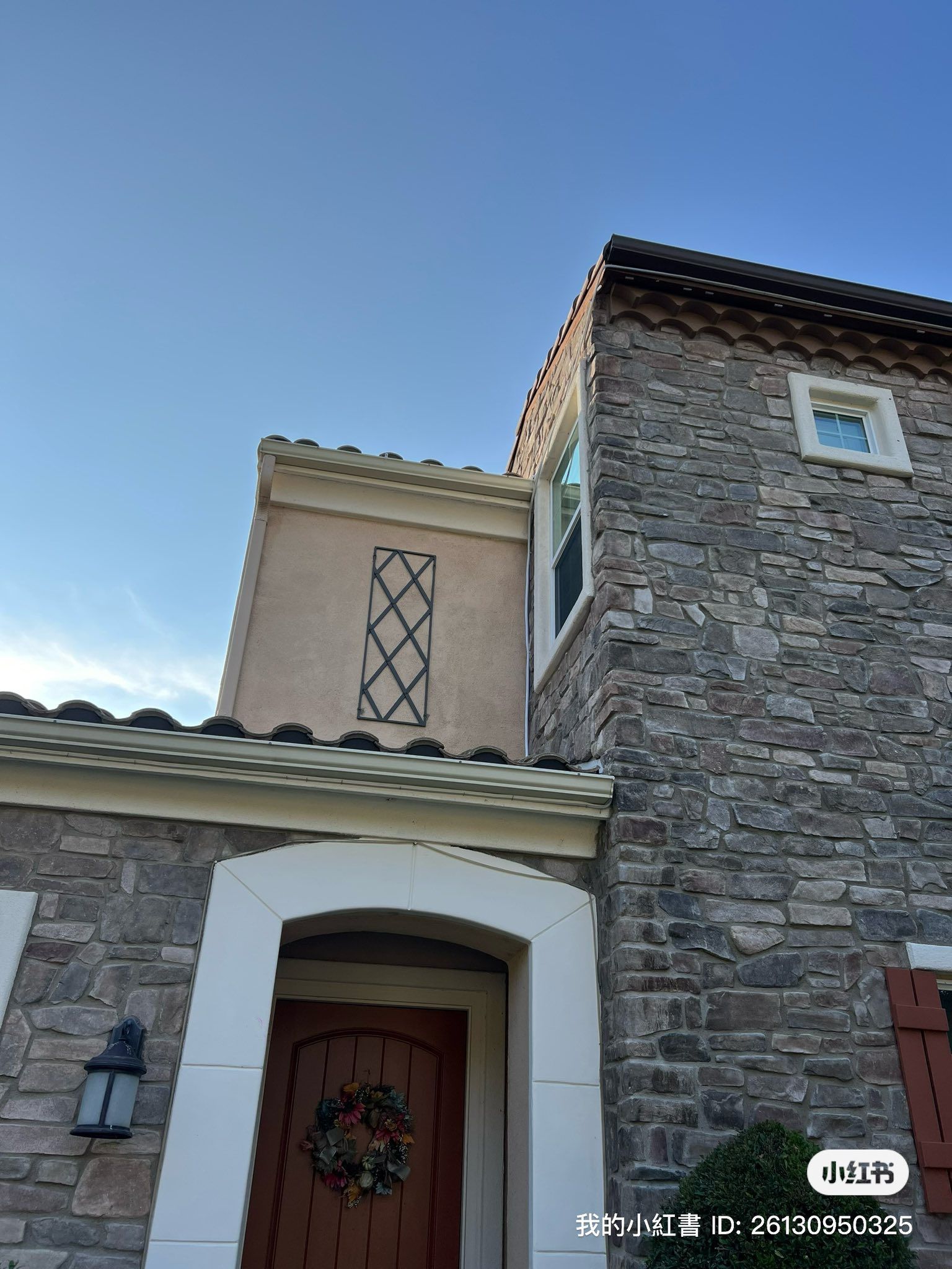 A two-story house exterior featuring stone facade, a stucco section with a metal trellis, and an arched entryway door.