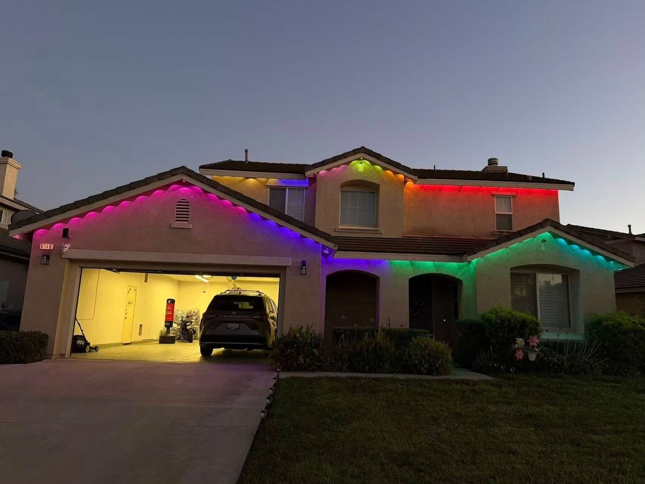 A two-story suburban home at dusk featuring festive, multi-colored LED lights outlining the roof eaves.
