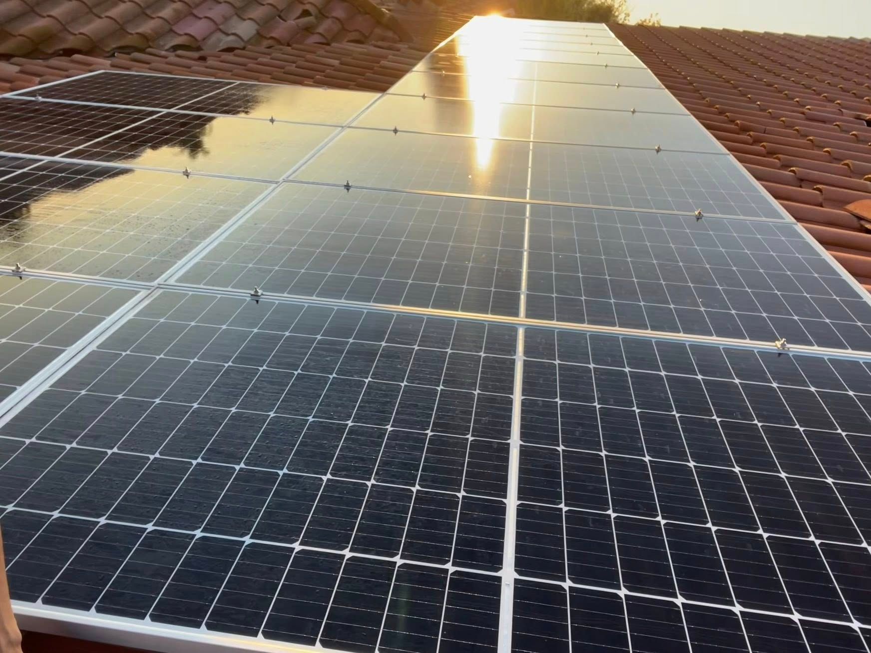 A close-up, angled view of dark solar panels installed on a terracotta tile roof during sunset.