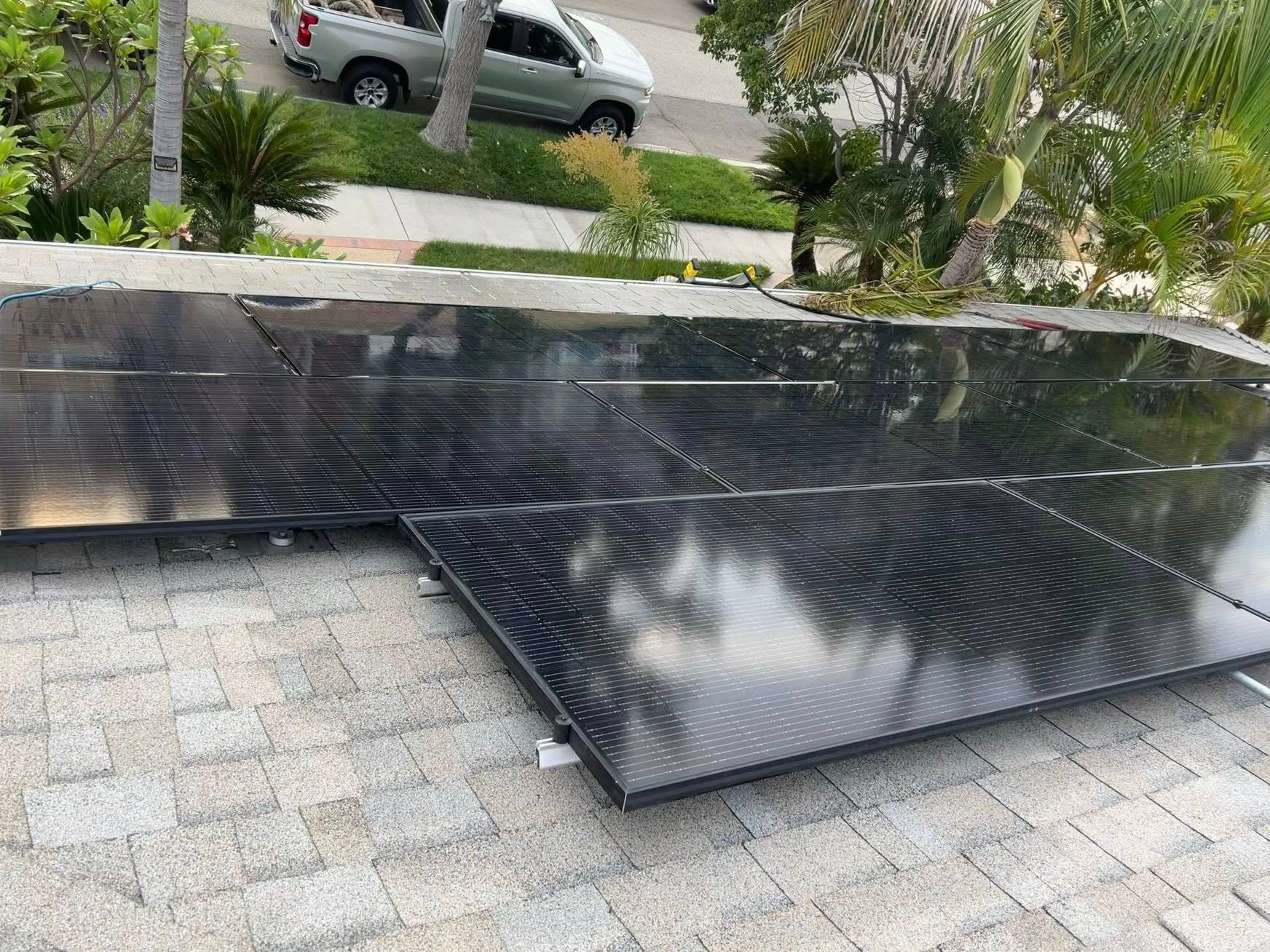 Black solar pool heating panels laid out on a paved driveway near a parked pickup truck and landscaped yard.