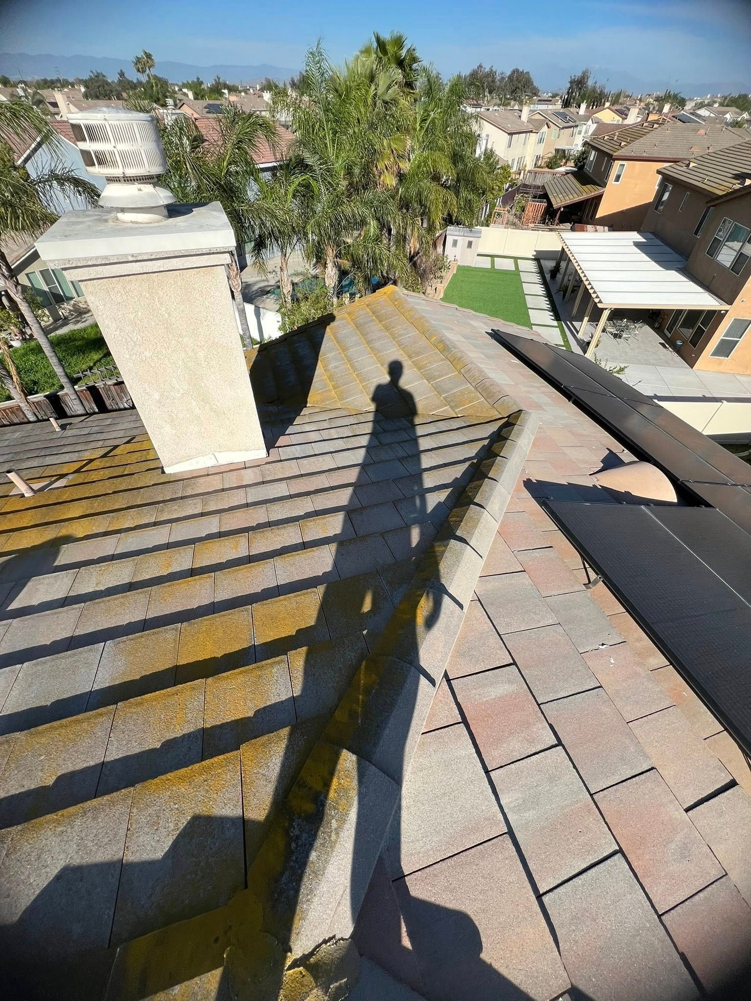 A high-angle view of a residential roof under construction, with a large chimney and the shadow of a person cast on tiles.
