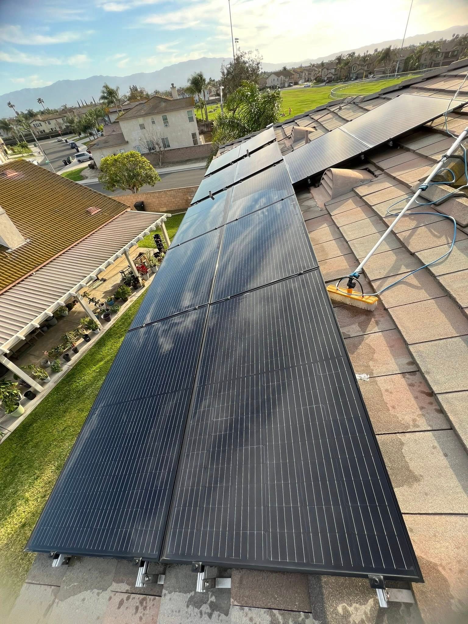 Black solar panels installed on a residential tile roof, with a suburban neighborhood in the background.