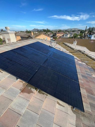 A black solar pool heating mat installed on a light-colored tile roof under a clear blue sky.