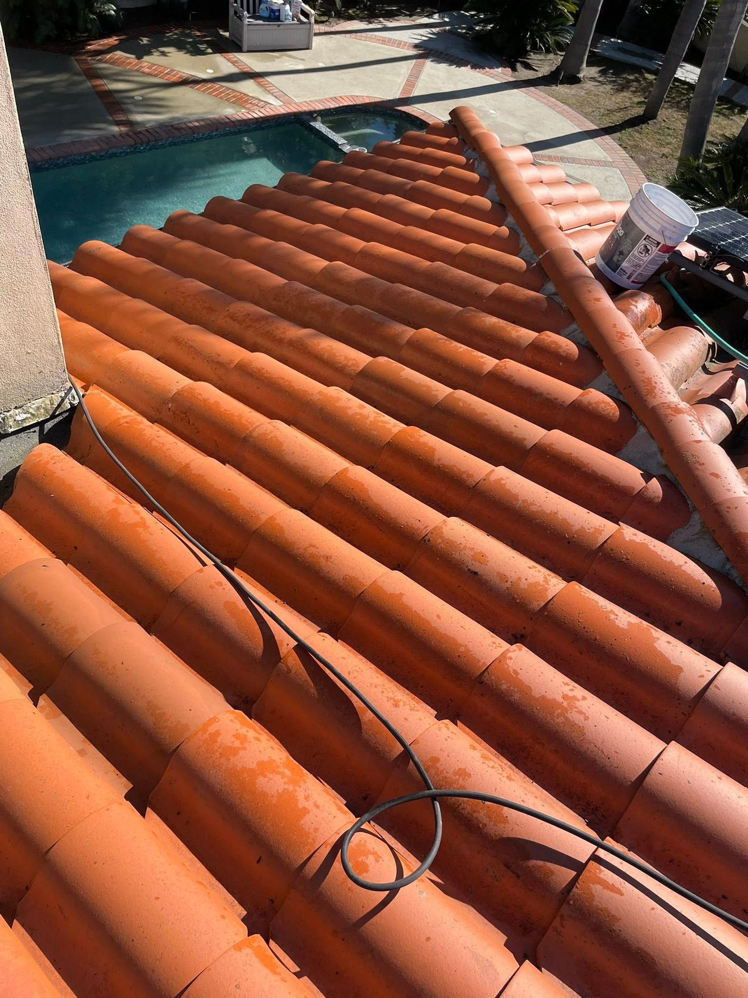 A high-angle view of a terracotta tile roof, with a garden hose resting on the tiles and a swimming pool visible below.