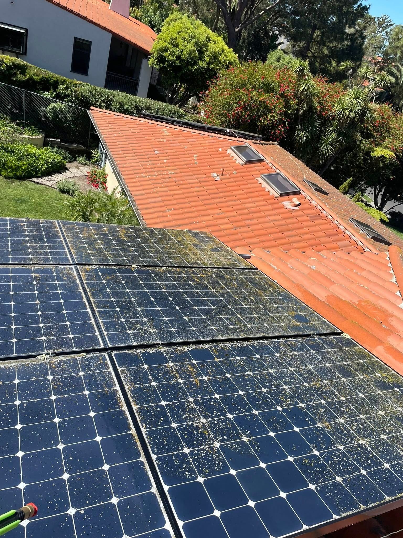 Solar panels covered in dirt and debris on a residential roof next to a tiled roof with two skylights.