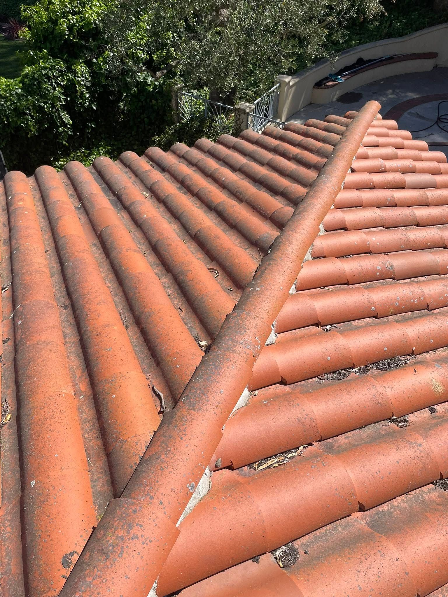 A close-up view of weathered, terracotta-colored roof tiles, with a single diagonal tile cutting across the pattern.