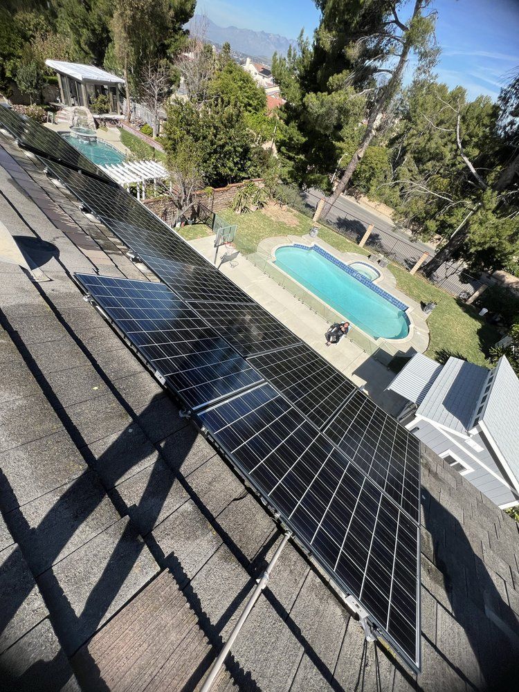 A high-angle view of solar panels mounted on a residential shingle roof, overlooking a backyard with a swimming pool.