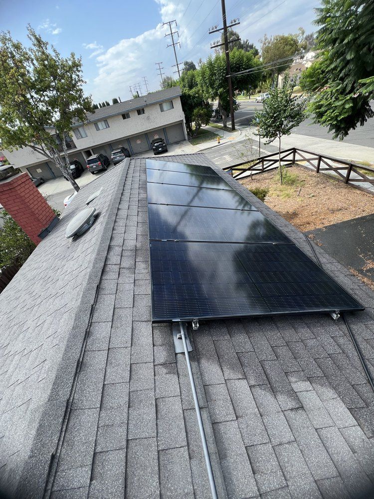 A residential asphalt shingle roof featuring a rectangular array of black solar panels with conduit running along the side.
