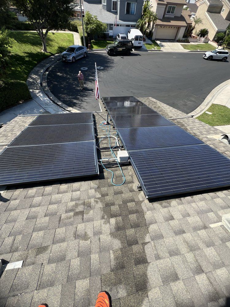 Two solar panel arrays installed on a residential shingled roof, viewed from above looking down toward a street.