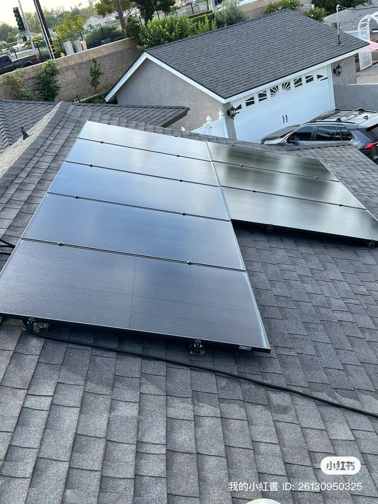 Solar panels installed on a dark shingled residential roof with a garage and driveway visible below.
