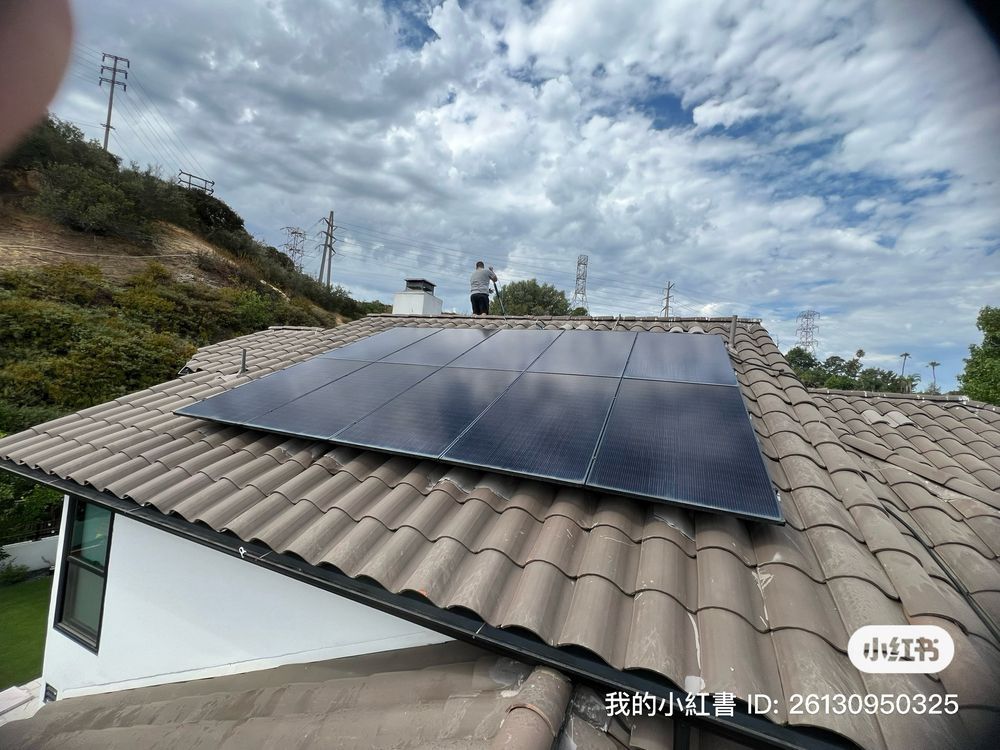 A rectangular array of dark solar panels installed on a residential tile roof under a cloudy sky.