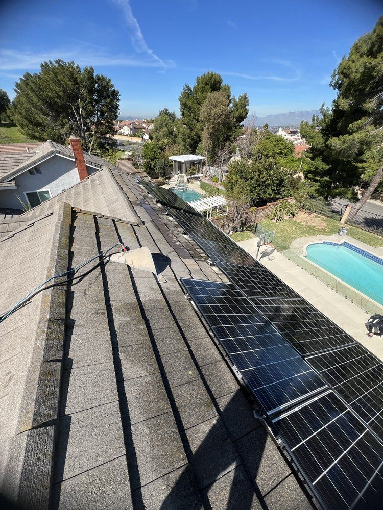 A high-angle view of a residential roof with black solar panels installed, overlooking a backyard with a swimming pool.