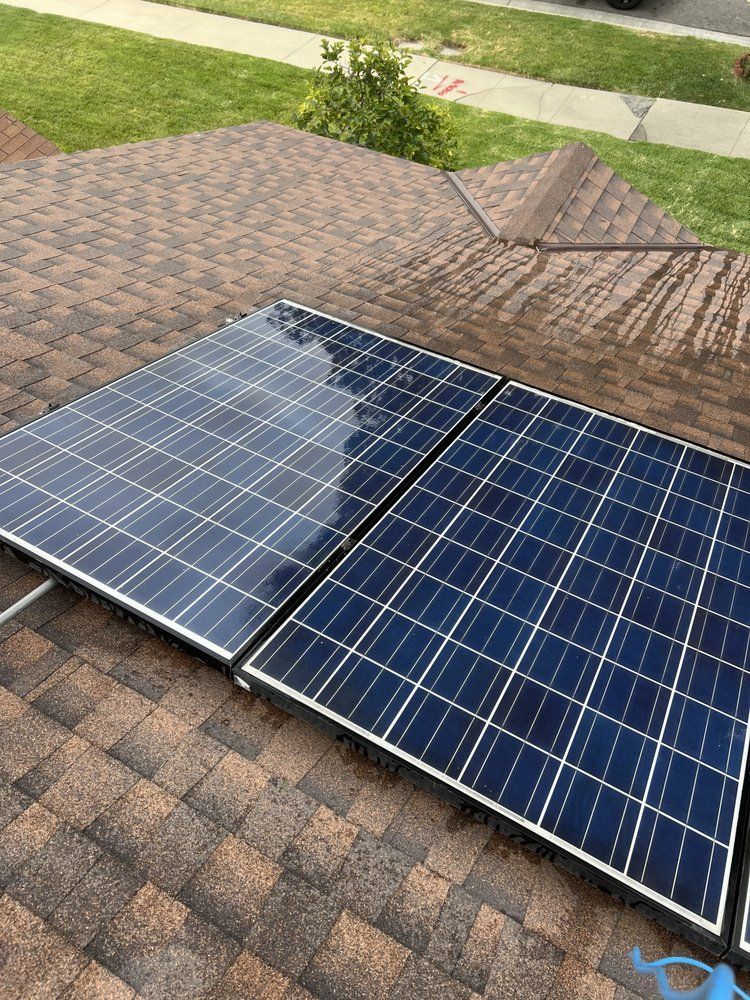 Two rectangular solar panels mounted on a brown shingled roof, with grass visible in the background.