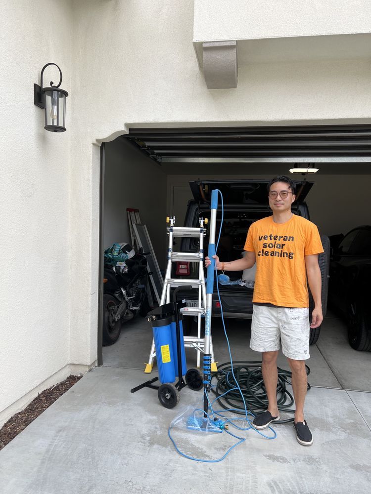 A professional cleaner in an orange shirt stands in a garage next to a ladder, water filtration tank, and cleaning pole.