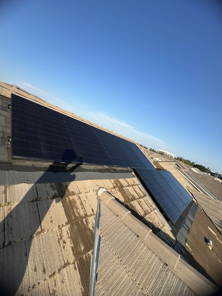Solar panels installed on a sloped, shingled roof under a bright blue sky.