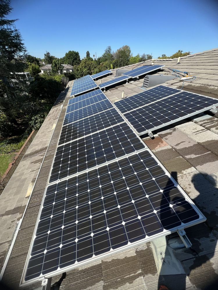A high-angle view of black solar panels installed in a grid pattern on a gray residential roof under a clear blue sky.