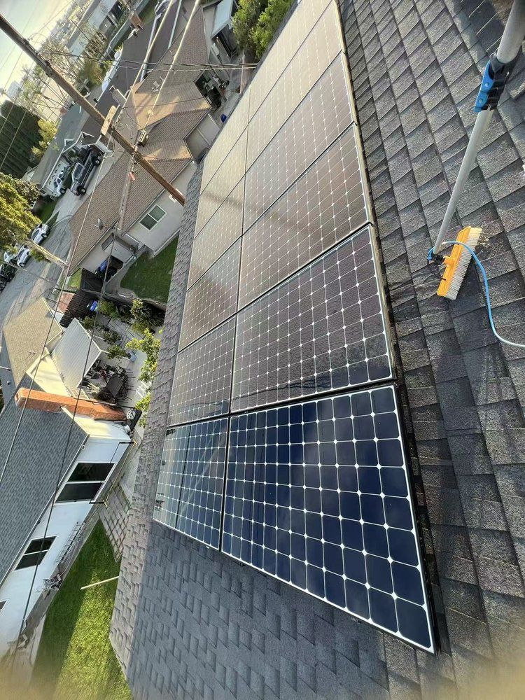 An elevated view of dark solar panels installed on a sloped shingle roof, with a cleaning brush visible on the right.