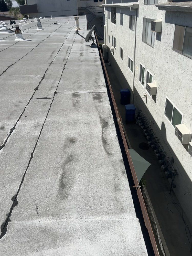 A flat gray roof adjacent to the side of a multi-story stucco apartment building with a narrow gap between them.