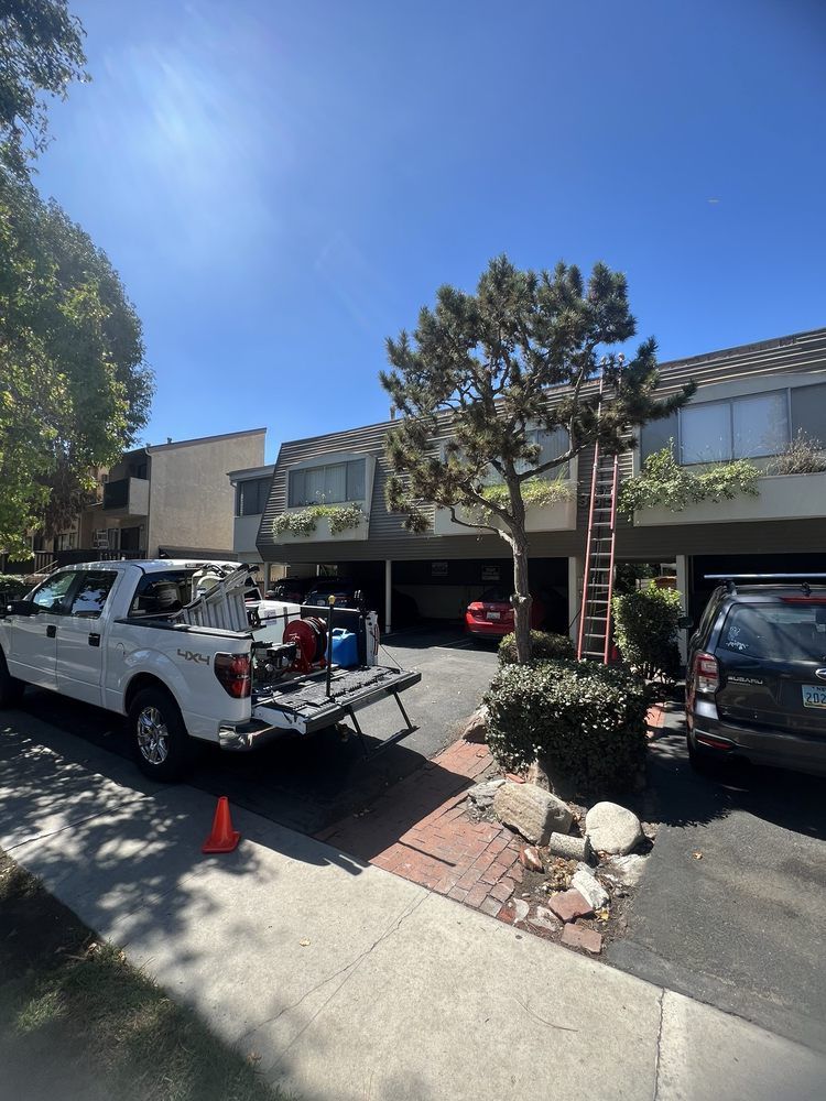 A white pickup truck parked in front of a multi-story apartment complex with a ladder leaning against the building.