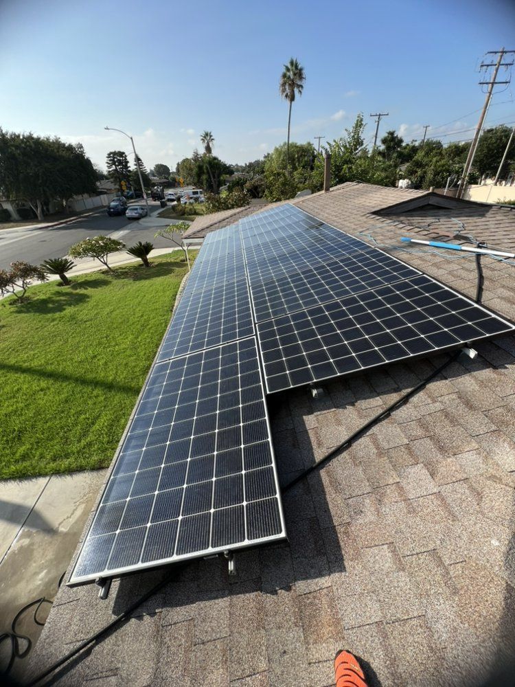 Rows of black solar panels installed on a residential shingled roof, view from above overlooking a green front lawn.