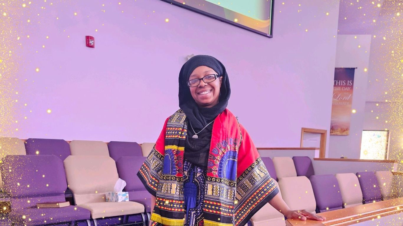 A woman wearing a hijab and glasses is standing in a room with purple chairs.