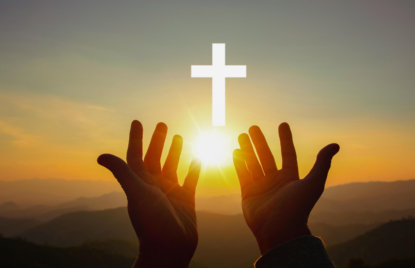 A person is praying with their hands up in front of a cross.