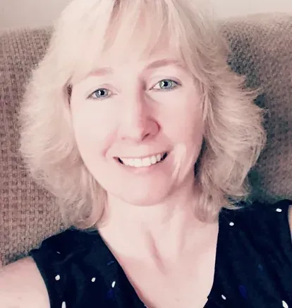 A woman with blonde hair is smiling while sitting in a chair.