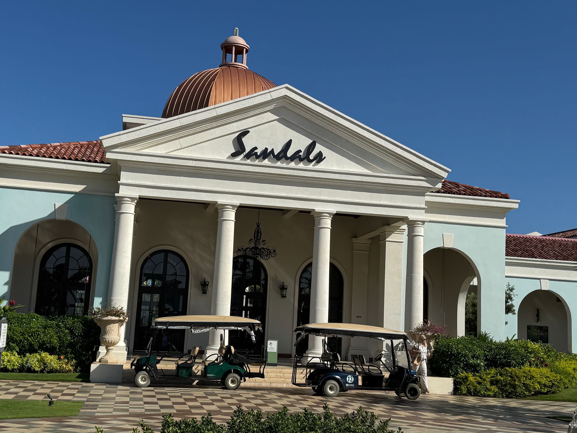 Sandals resort entrance with golf carts parked in front; blue sky.