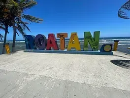 A colorful sign that says roatan on a beach with palm trees in the background.