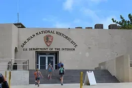 A group of people are walking up the stairs to the san juan national historic site.