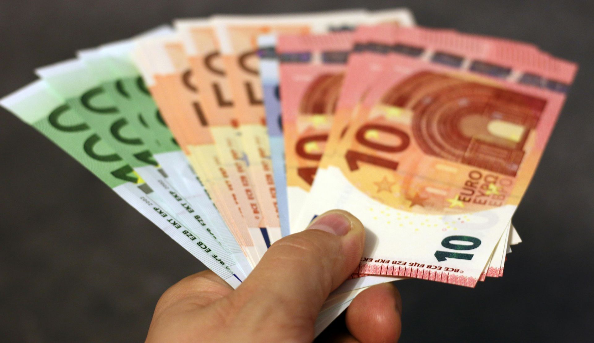 A person is holding a fan of euro bills in their hand