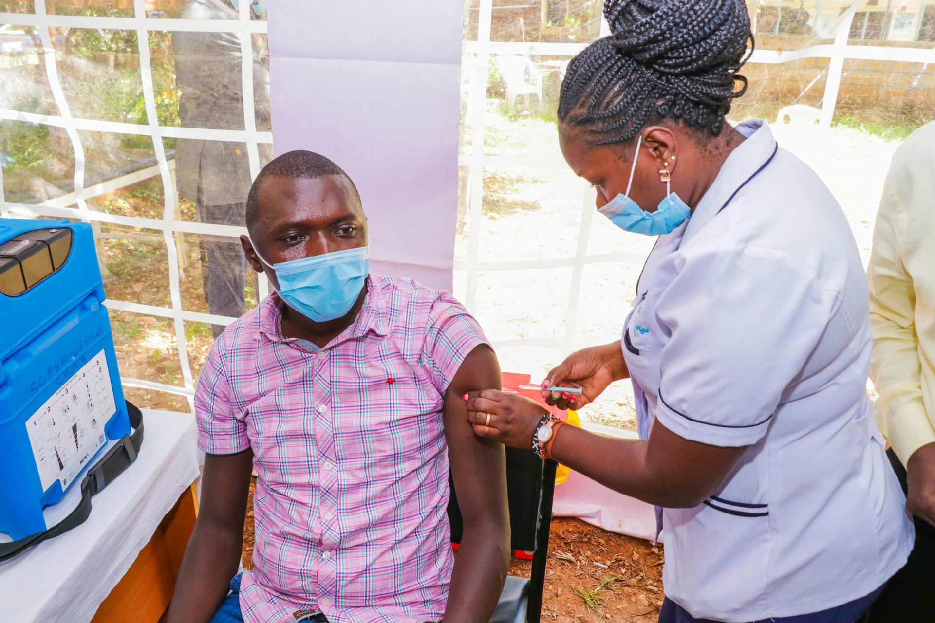 A man wearing a mask is getting a vaccine from a nurse.