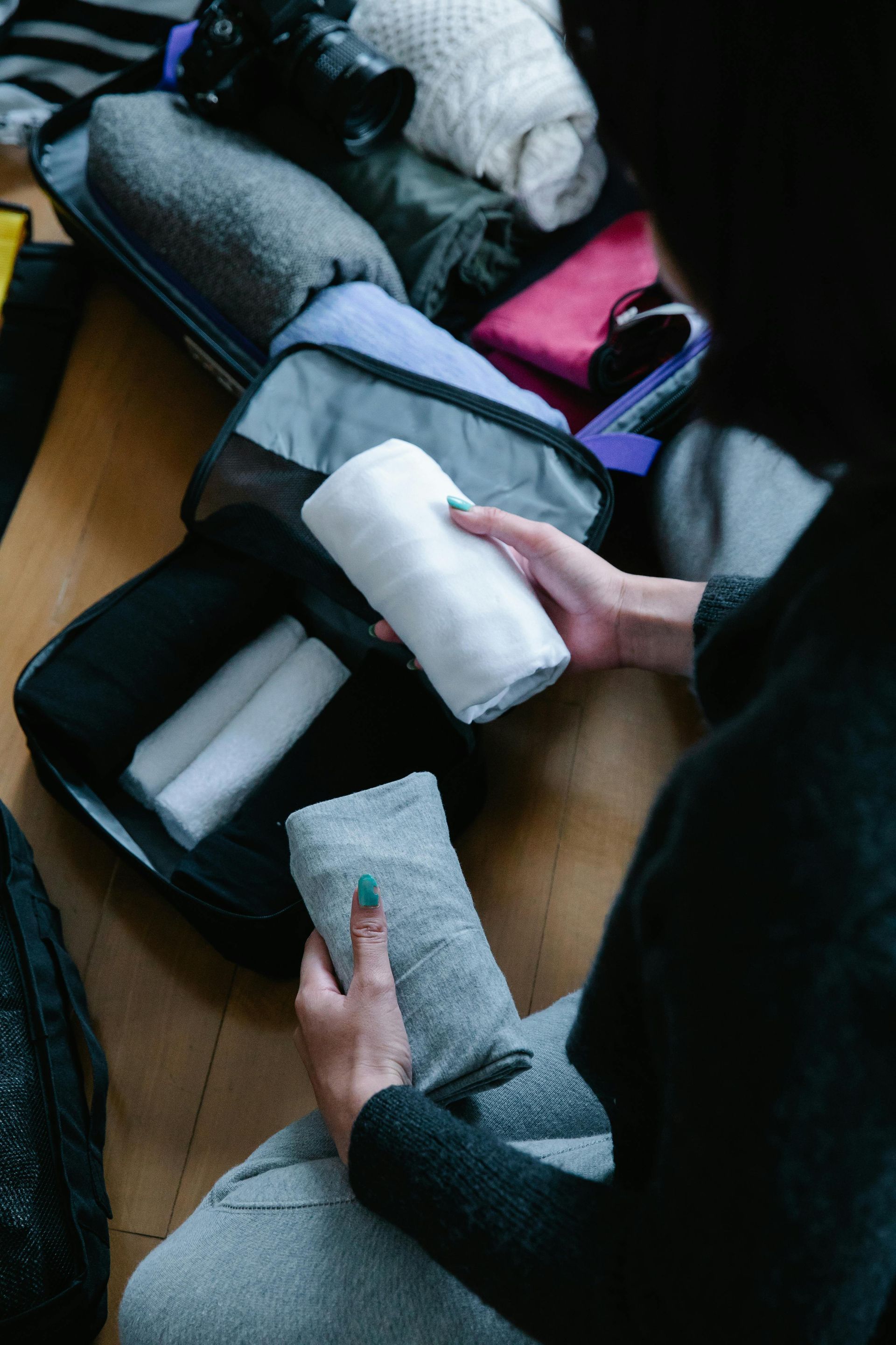 A woman is sitting on the floor packing a suitcase.