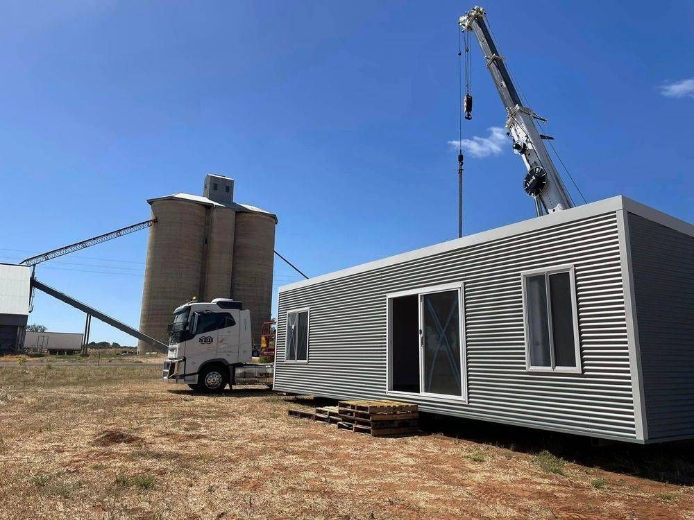 A crane is lifting a container house in a field.