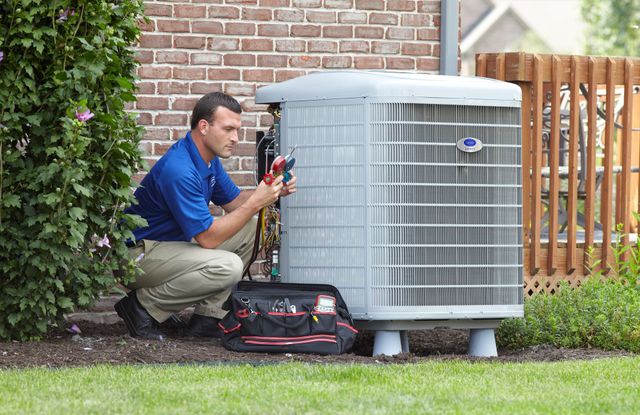 HVAC technician servicing an air conditioner outside, using tools and a pink refrigerant tank.