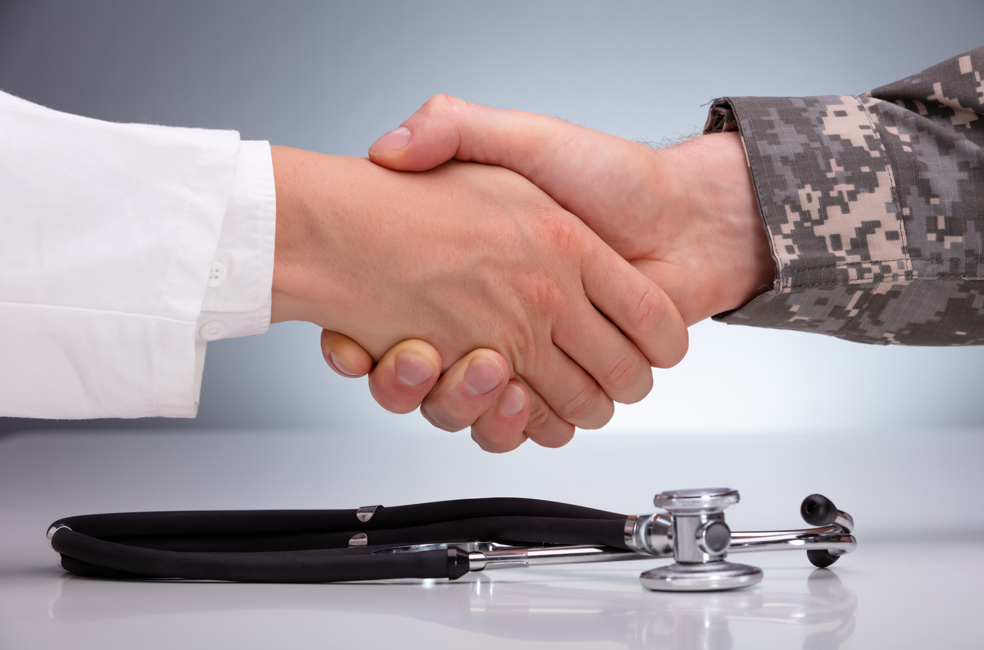 A doctor and a soldier are shaking hands in front of a stethoscope.