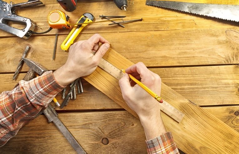 A Person is Measuring a Piece of Wood With a Ruler — Mick's Carpentry & Maintenance In Machans Beach, QLD