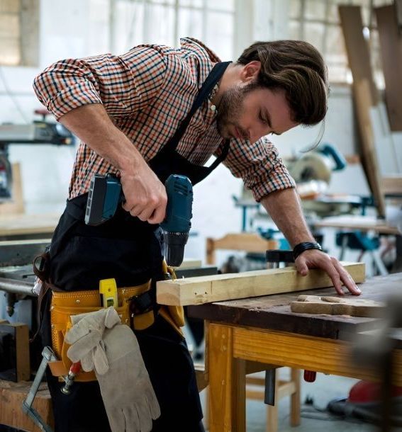 A Man is Using a Drill on a Piece of Wood — Mick's Carpentry & Maintenance In Machans Beach, QLD
