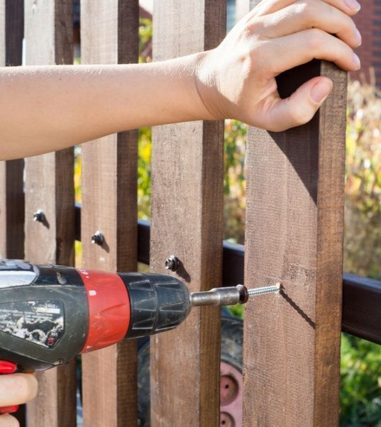 A Person is Installing a Wooden Fence With a Drill — Mick's Carpentry & Maintenance In Machans Beach, QLD