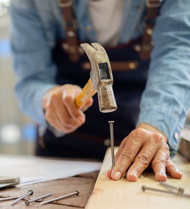 A Man is Hammering a Nail Into a Piece of Wood — Mick's Carpentry & Maintenance In Machans Beach, QLD